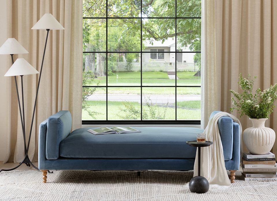 Serene contemporary daybed with navy upholstery and wood legs, framed by floor-to-ceiling windows and neutral drapery.