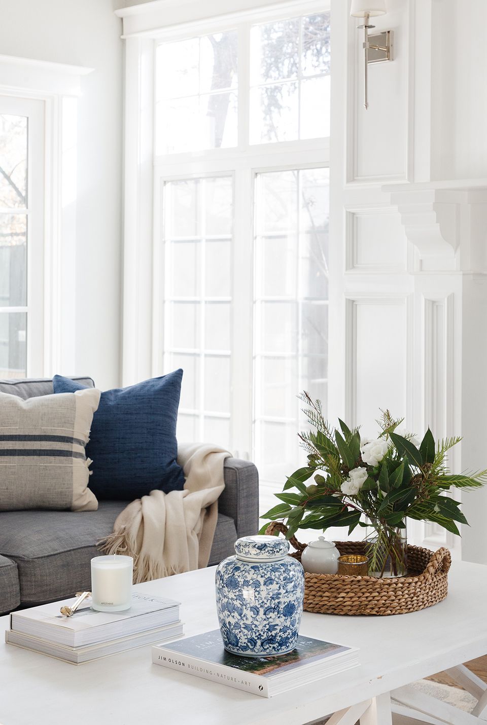 Bright transitional living room: white trim and doors, gray sofa, navy accent pillow, blue ceramic vessel, greenery.