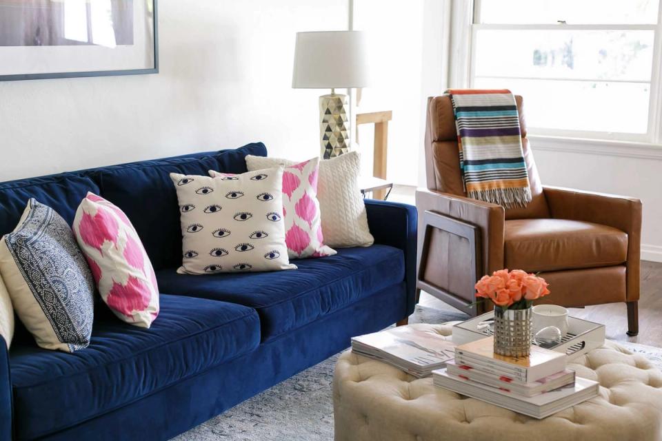 Contemporary living room with navy velvet sofa, cognac leather chair, and pops of pink in eclectic pillows