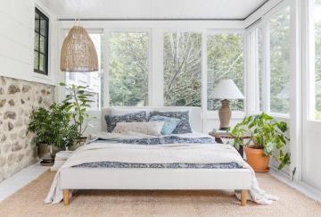 Serene sunroom bedroom with potted plants, blue accents, and abundant glass walls