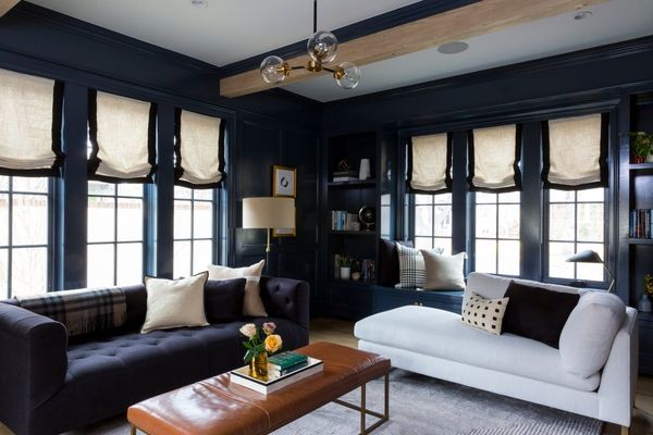 New Classic living room with navy walls, natural wood beam, brass pendant light, and mix of dark and light upholstered seating