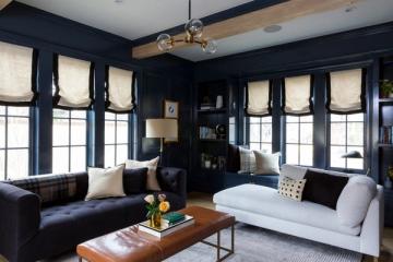 New Classic living room with navy walls, natural wood beam, brass pendant light, and mix of dark and light upholstered seating