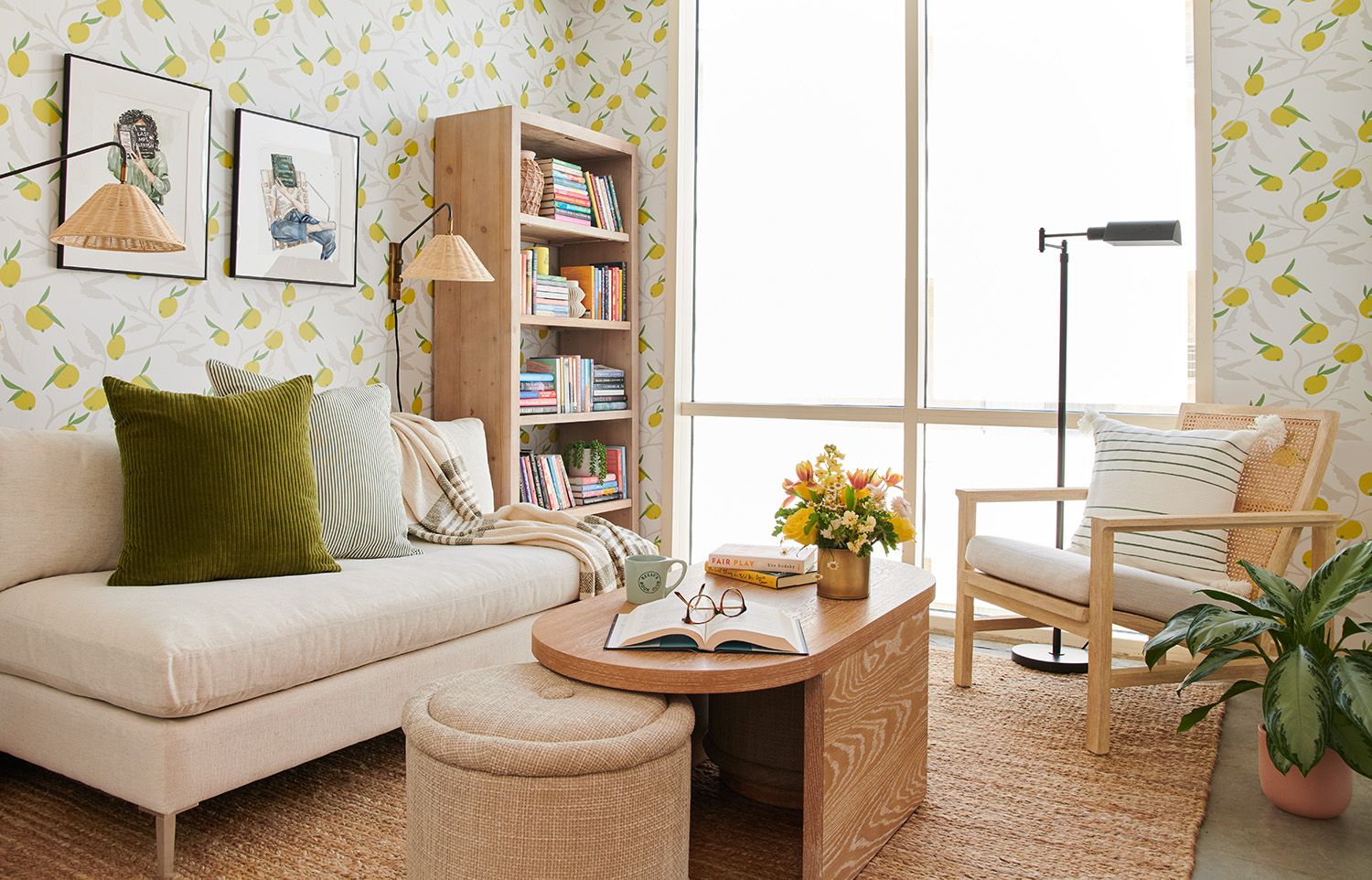 Bright reading room with lemon-print wallpaper, cream sectional, natural wood shelving, and abundant natural light