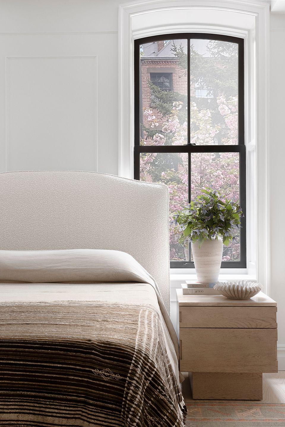 Tranquil modern bedroom with cream upholstered bed, arched window, and soft natural light