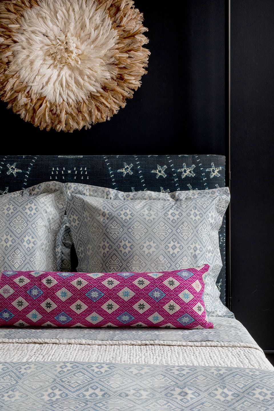 Textured bedding detail with magenta geometric lumbar pillow, woven wall hanging, and dark moody backdrop