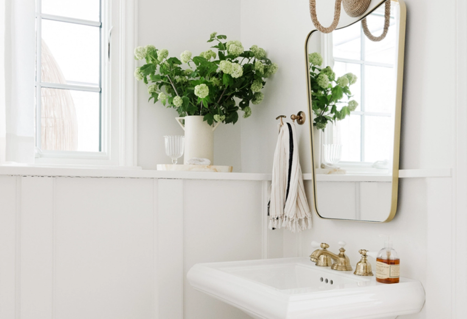 Serene spa bathroom with white shiplap, fresh greenery, brass fixtures, and natural light creating a calming wellness retreat.
