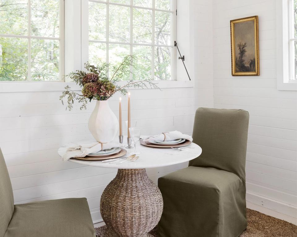 Bright cottage dining nook with olive green chairs, white round table, and natural dried florals