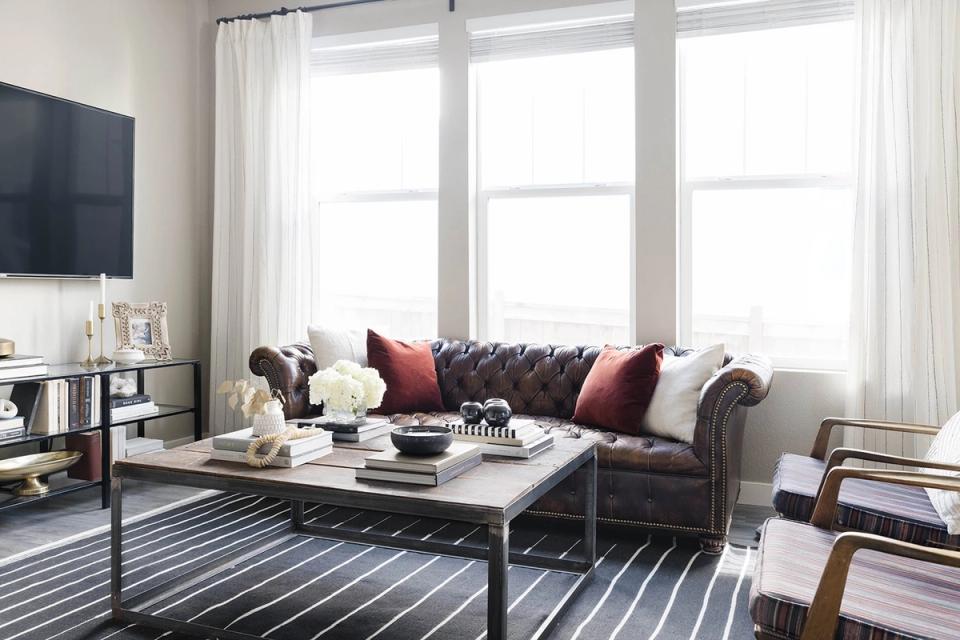 Transitional living room with charcoal sectional, burgundy accent pillows, striped area rug, and bold dark accents against bright windows