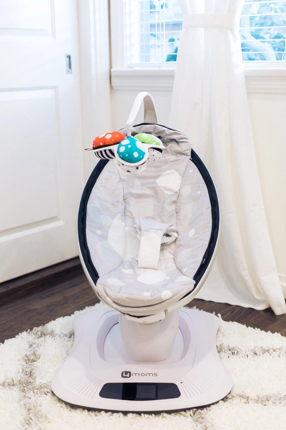 Modern white baby rocker by bright windows with colorful toys, minimalist nursery aesthetic