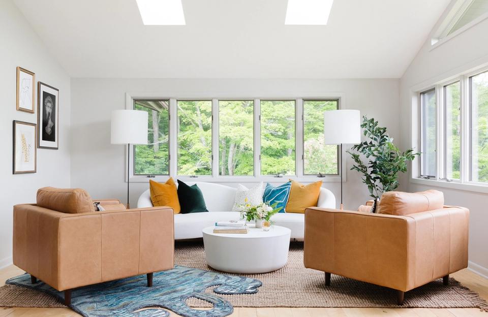 Airy dopamine-forward living room with caramel leather chairs, blue accents, and bright windows