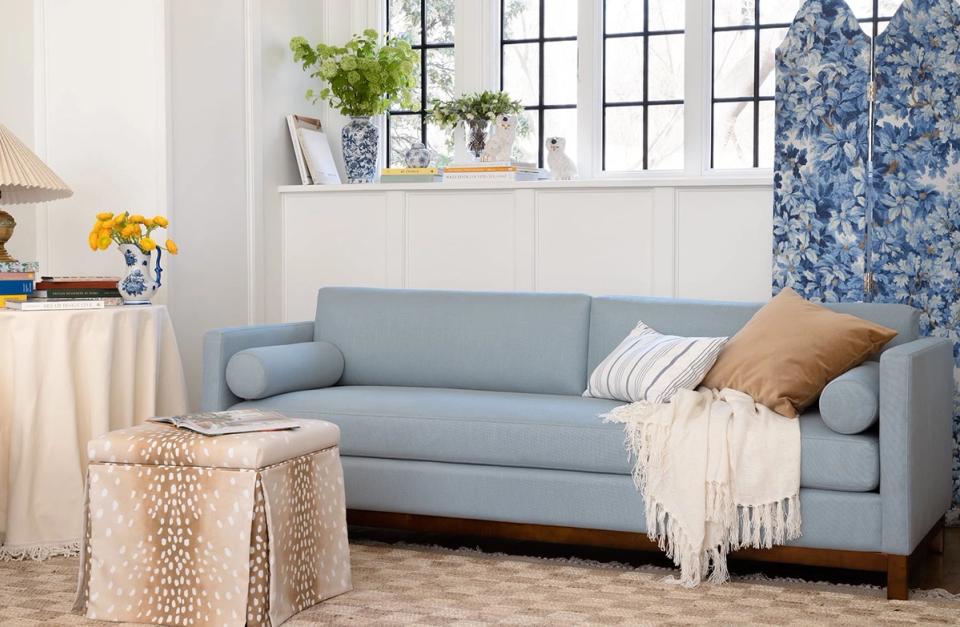 Airy cottage-style room with soft blue curved sofa, natural textures, and blue botanical accents