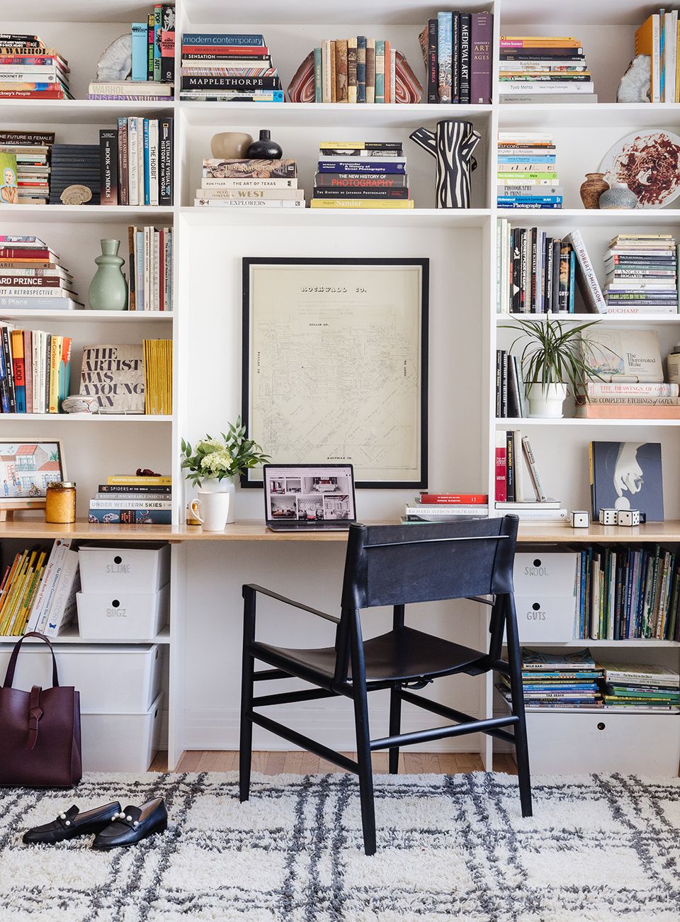 Eclectic white shelving workspace with colorful book collection, black chair, and patterned rug