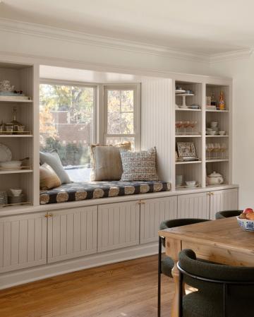 Airy farmhouse kitchen with cream beadboard cabinetry and cozy window seat with patterned cushions