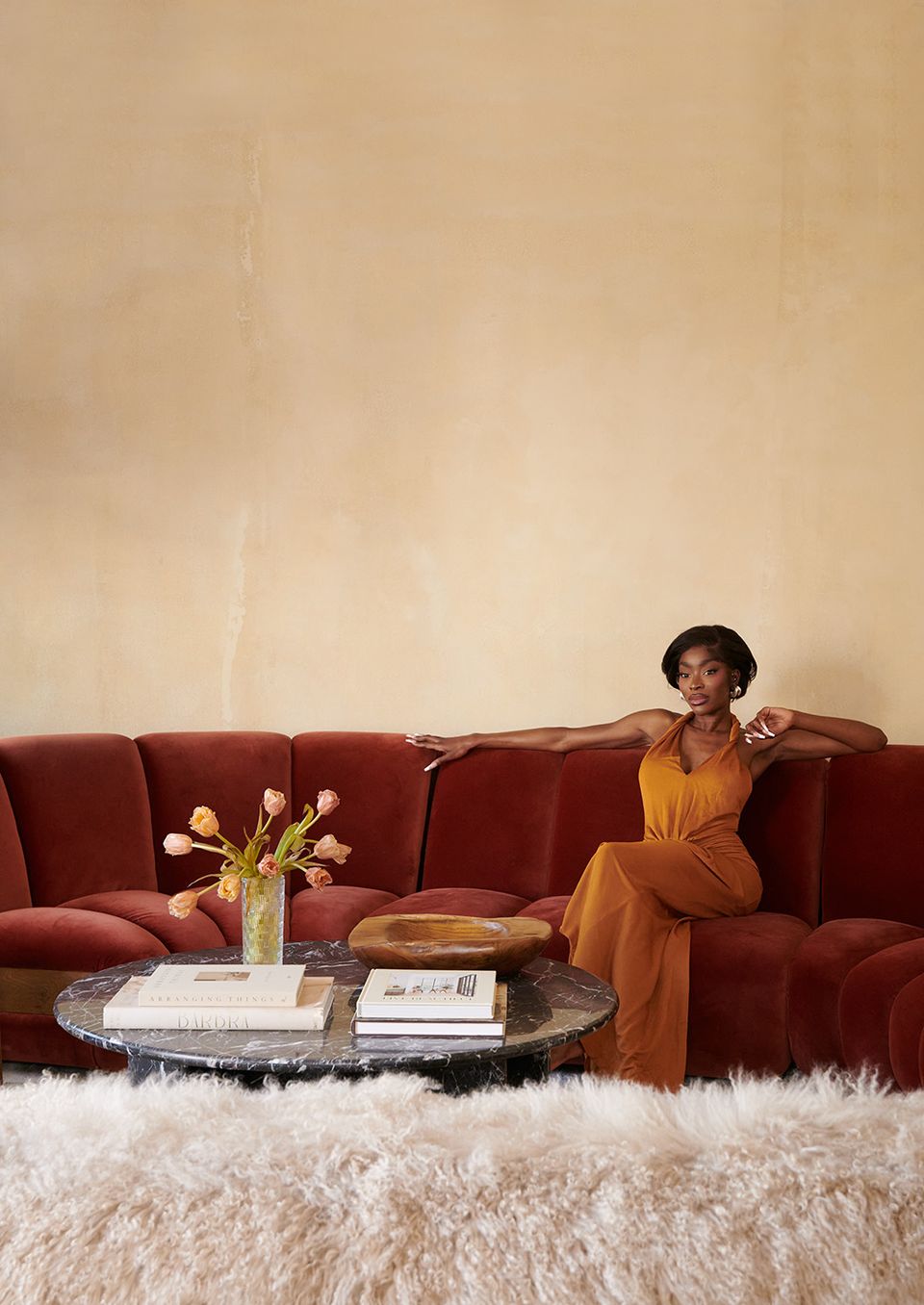 Rich jewel-toned burgundy curved sofa against minimalist cream backdrop, accented with warm mustard tones and soft textures