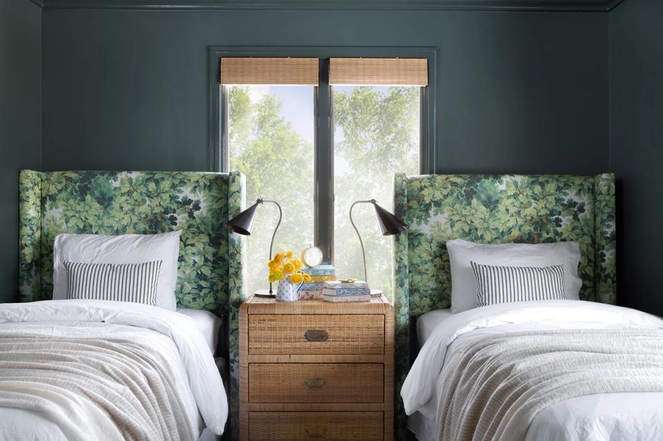 Spa-inspired twin bedroom with muted teal walls, verdant upholstered headboards, warm wood nightstand, and airy striped pillows