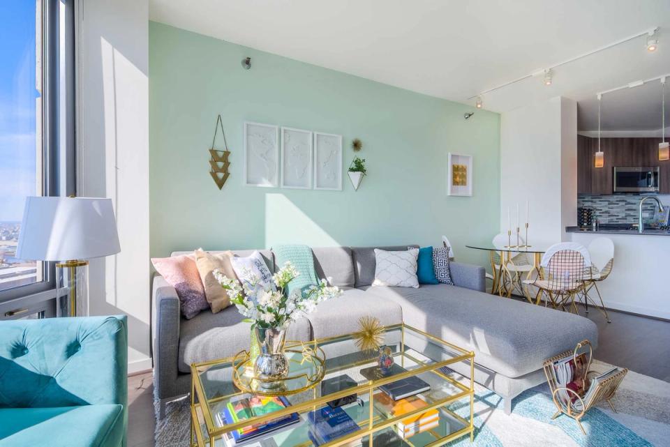 Serene modern space with soft mint walls, neutral sectional, geometric brass coffee table, and airy natural lighting