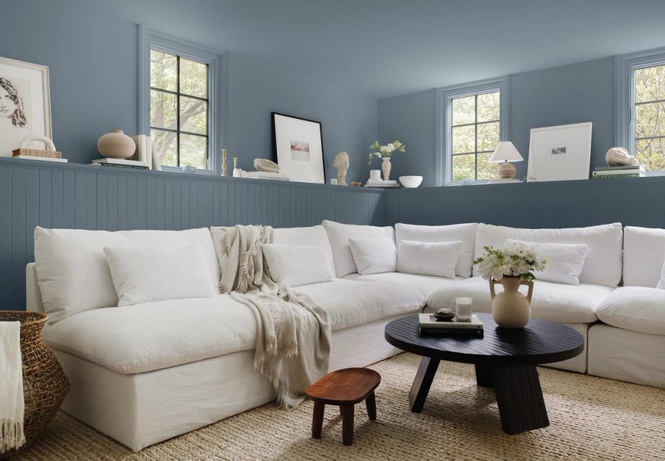 Serene blue-gray living room with cream sectional, black round table, and calming coastal aesthetic