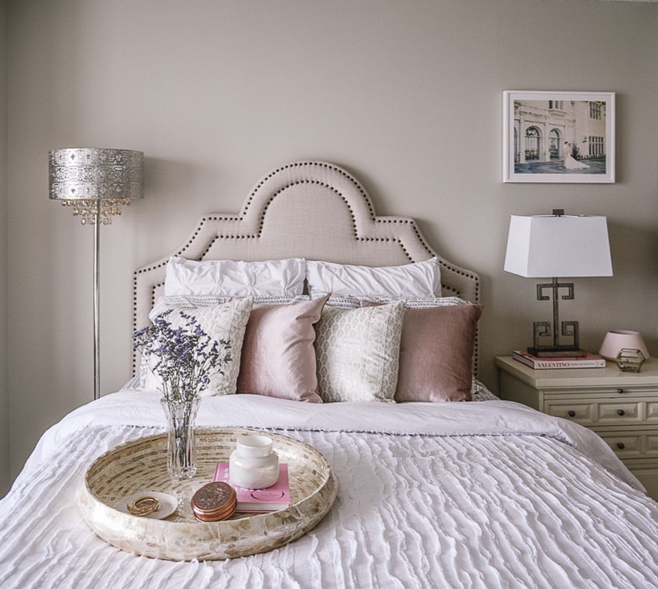 Soft romantic bedroom with blush pink accents, neutral upholstered headboard, and layered bedding in warm metallics