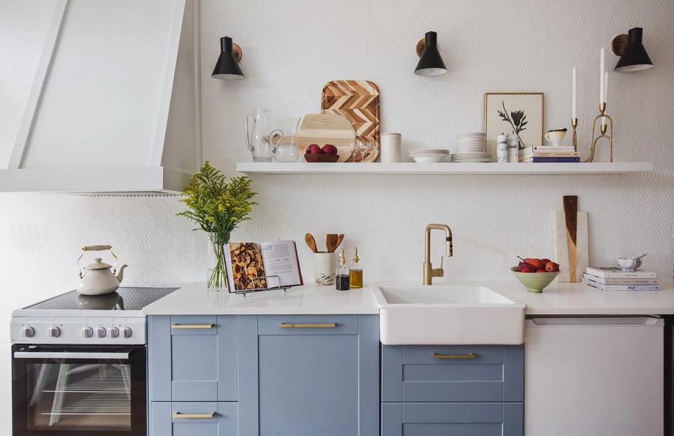 Contemporary kitchen with soft blue-gray cabinets, white countertop, floating shelves, and industrial black pendants.