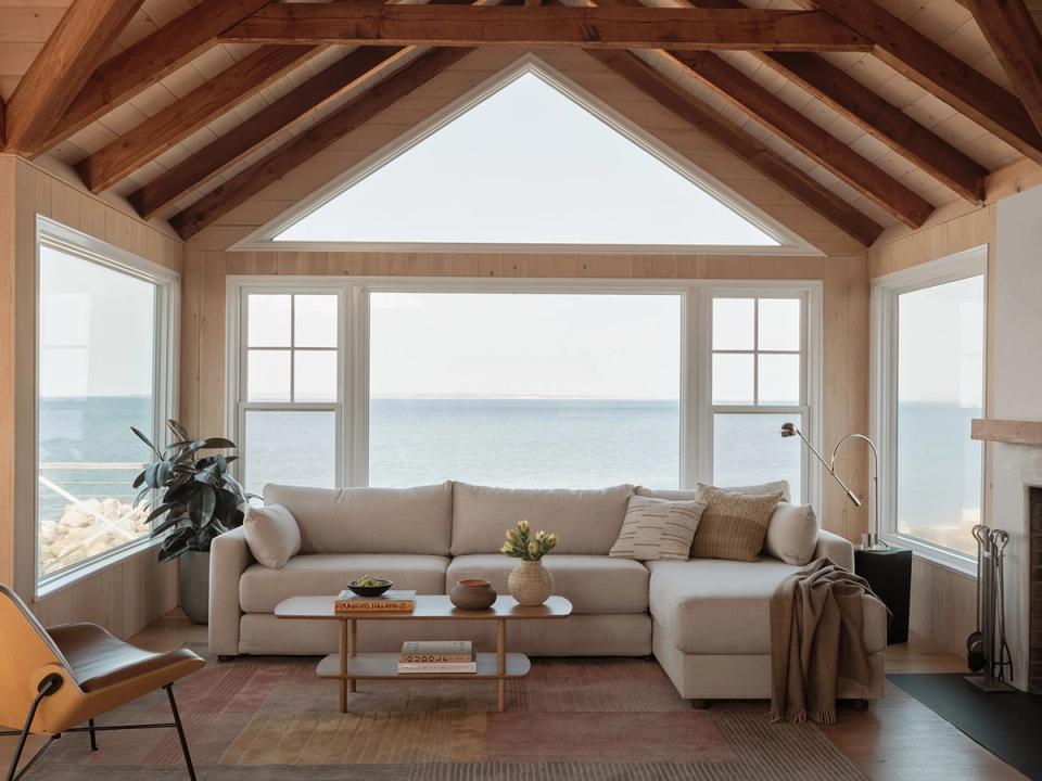 Coastal modern retreat with beige sectional, exposed timber ceiling, ocean views, and warm earthy palette