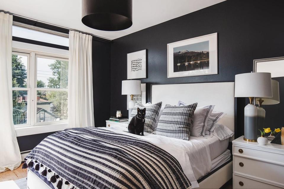 Modern moody bedroom with charcoal walls, striped bedding, and bright natural light from large windows creating high-contrast sophistication