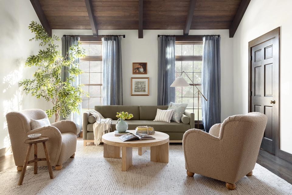 Neutral farmhouse living room with conversational seating layout, beige and olive tones, natural wood coffee table, and soft blue window treatments