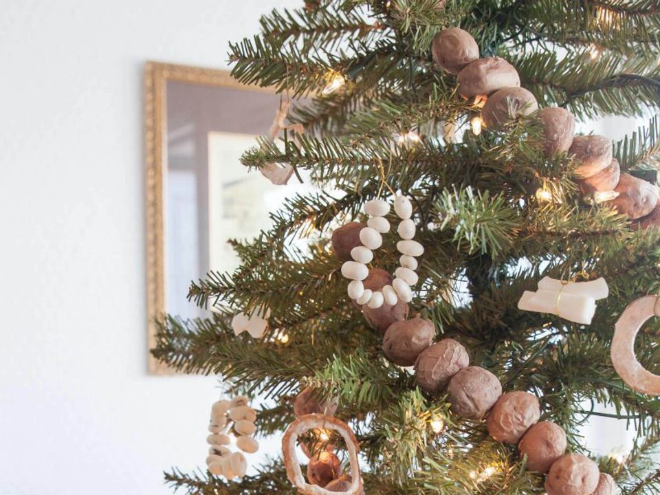 Modern minimalist Christmas tree with mauve and blush felt ball garlands, natural wood ornaments, and warm gold accents against white wall