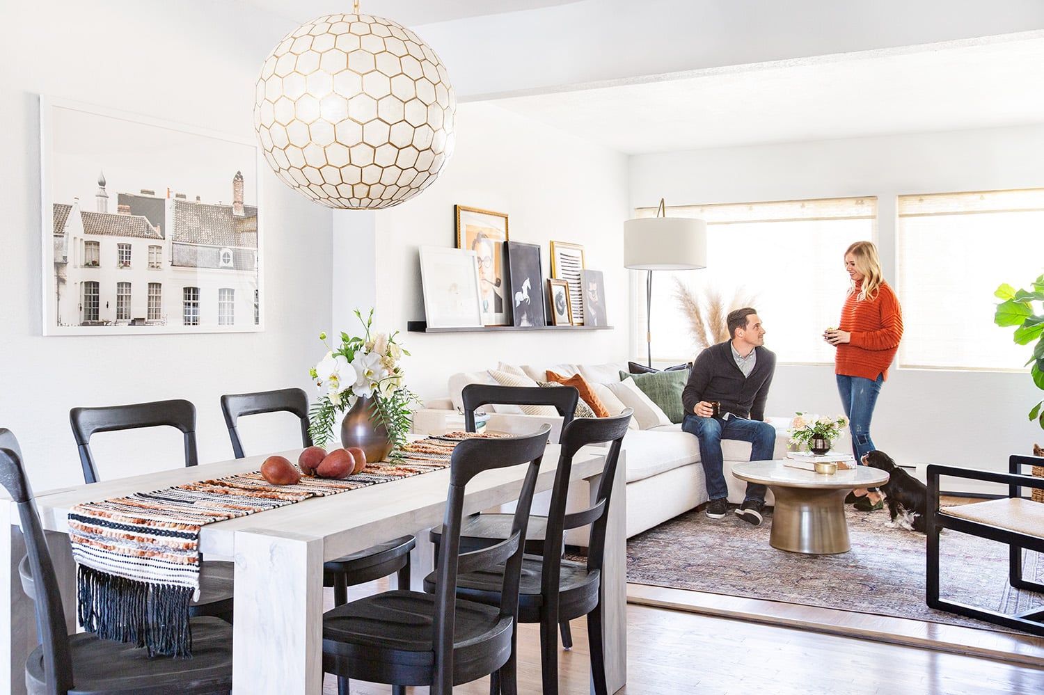 Bright modern dining space with geometric pendant light, white table, black chairs, and neutral palette