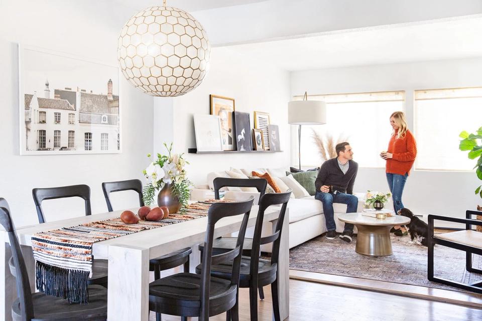 Bright modern dining space with geometric pendant light, white table, black chairs, and neutral palette