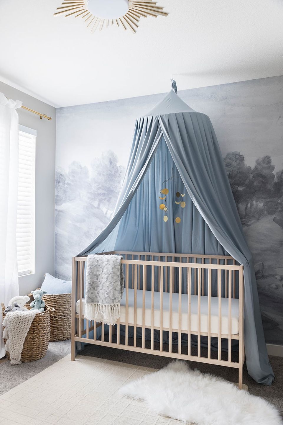 Serene nursery with blue canopy, landscape mural backdrop, natural wood crib, and soft gold accents
