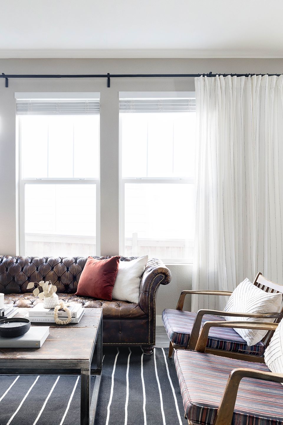 Bright transitional seating area with tufted sofa, striped rug, sheer curtains, and mid-century wooden chair