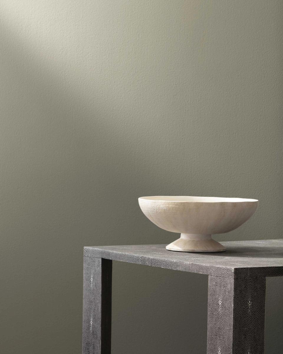 Minimalist aesthetic with muted sage green walls and sculptural cream bowl on concrete table