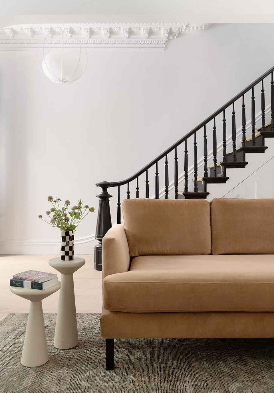 Minimalist entryway pairs warm caramel sofa with black staircase, botanical touches, and airy white molding for sophisticated ease