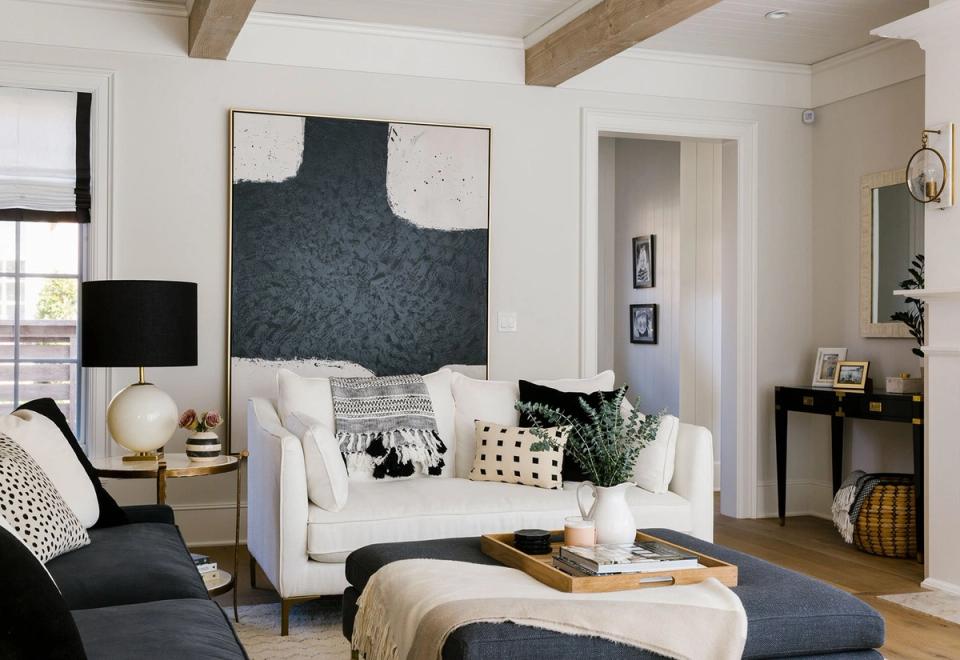 Scandinavian living room with cream sofa, black accents, geometric wall art, and warm wood beams creating cozy, minimalist elegance.
