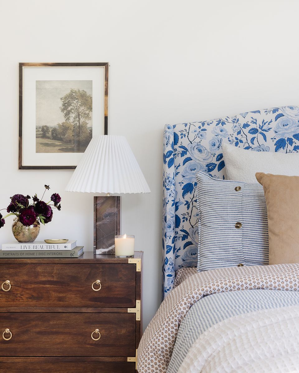 Master bedroom with blue-and-white patterned headboard, wood nightstand, vintage landscape print, and warm bedding