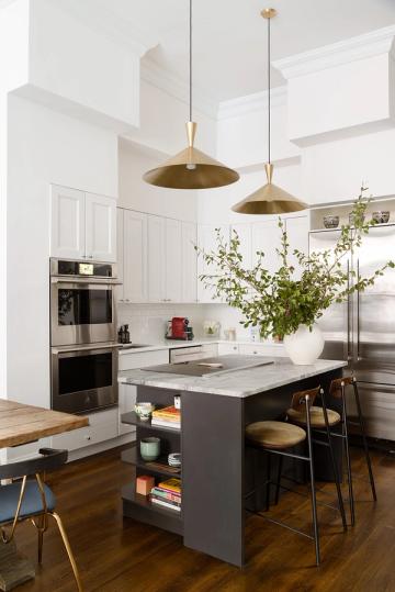 Modern farmhouse kitchen with white shaker cabinets, gray island, brass pendants, and hanging greenery