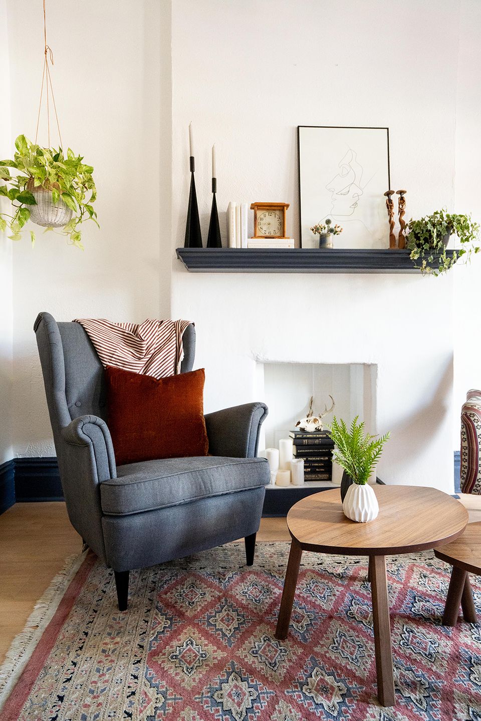 Eclectic modern corner with charcoal wingback chair, deep red velvet pillow, floating shelf styling, and vintage patterned rug for warmth