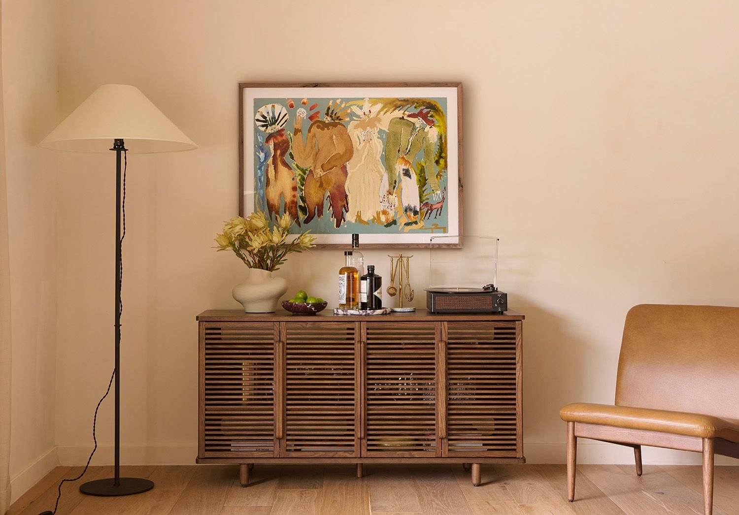 Warm mid-century living room with slatted wood credenza, floor lamp, and framed botanical art creating a cohesive, organized aesthetic.