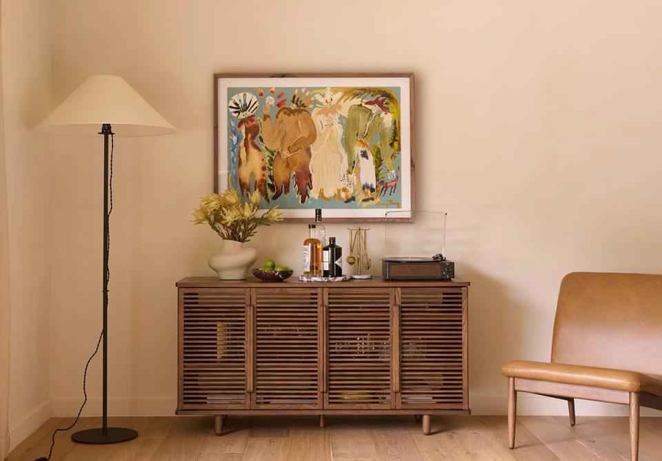Warm mid-century living room with slatted wood credenza, floor lamp, and framed botanical art creating a cohesive, organized aesthetic.