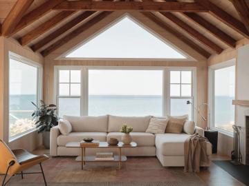 Coastal living room with exposed wood beams, neutral sectional, and panoramic ocean views through large windows
