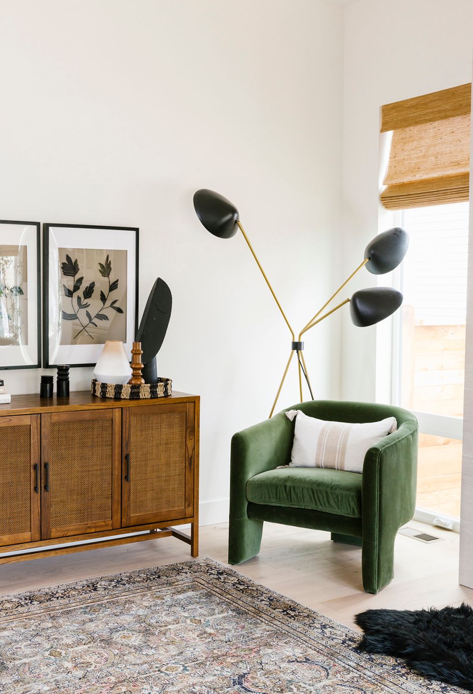 Mid-century modern living room with warm wood sideboard, emerald green armchair, and sculptural brass floor lamp against serene white walls