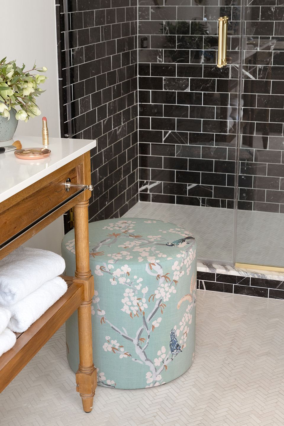 Spa-inspired bathroom with black subway tile shower, warm wood vanity, sage floral ottoman, and natural wood accents