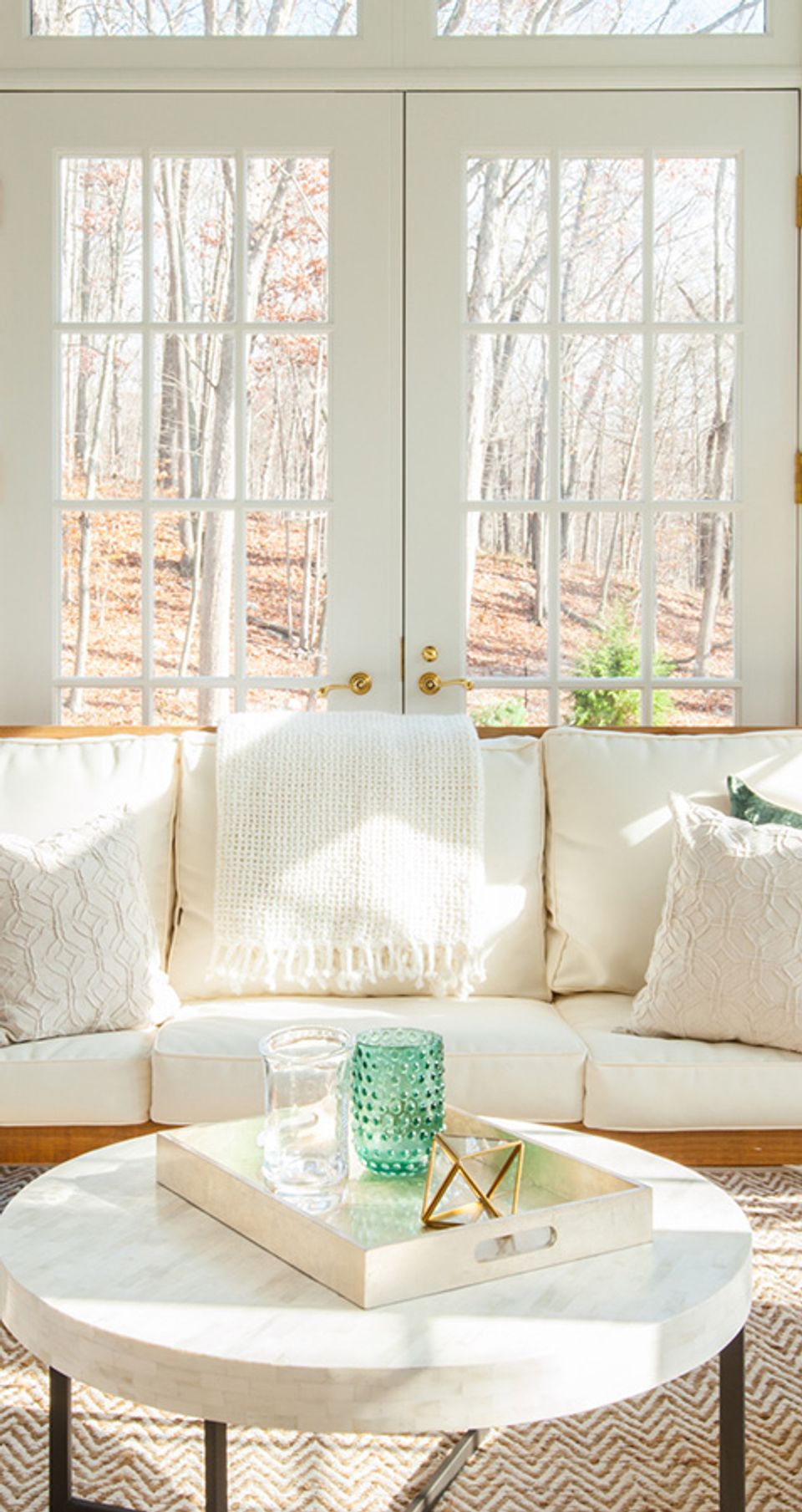 Bright sunroom with cream sofa, natural light from grid windows, soft neutral palette with green accents