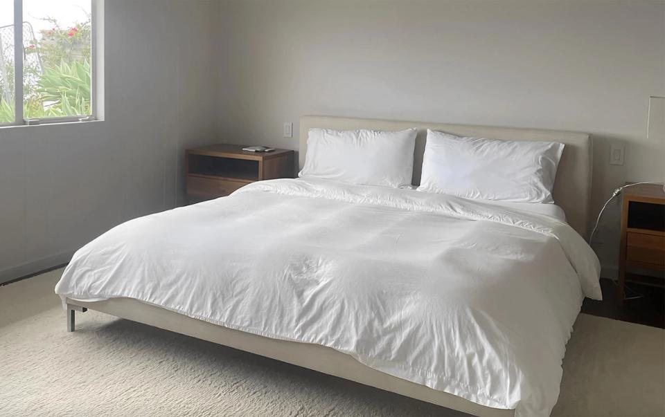 Calm minimalist bedroom with soft gray walls, crisp white linens, and natural light from windows