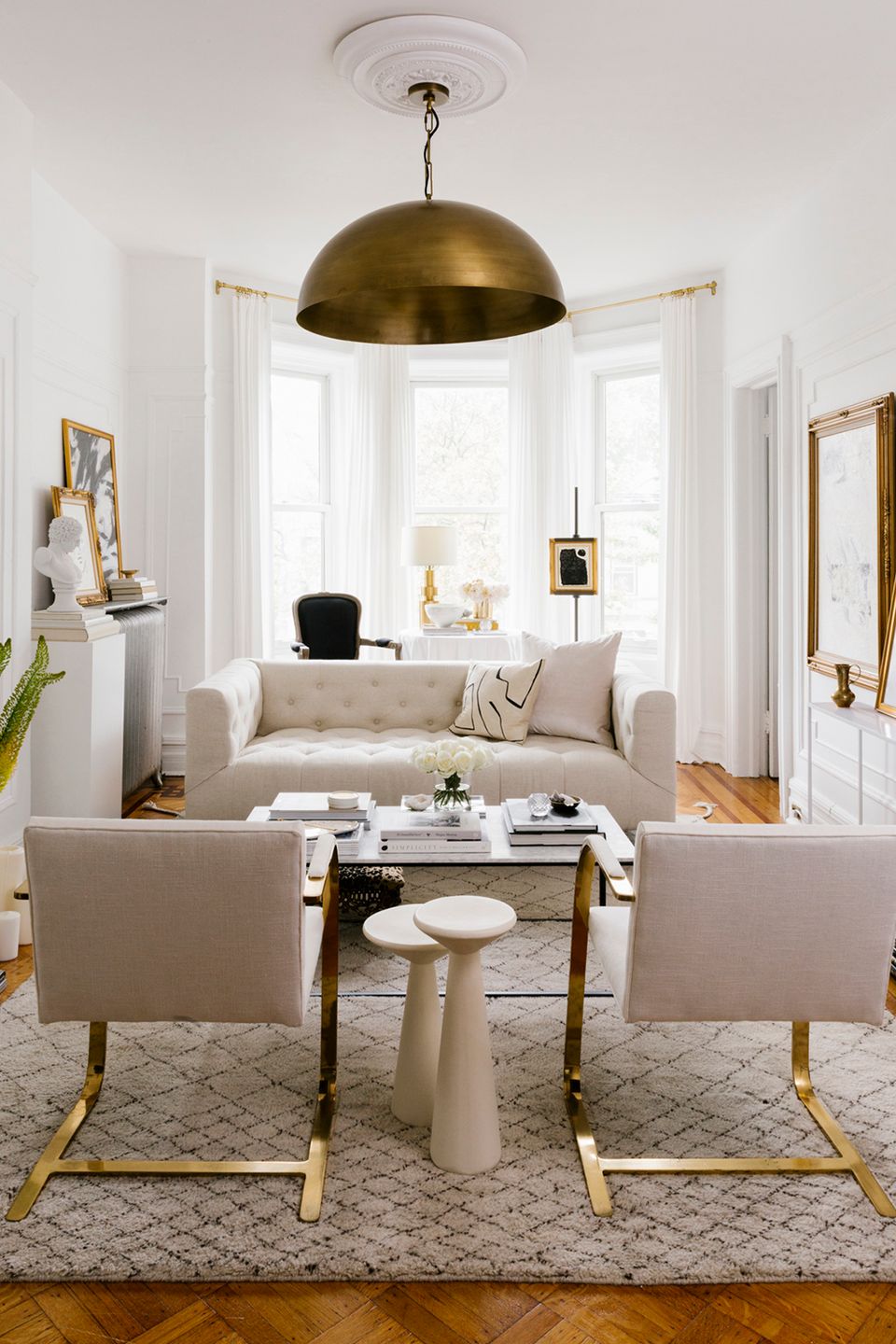 Minimalist small seating area with brass dome pendant, cream upholstery, and gold-accented furniture in bright natural light