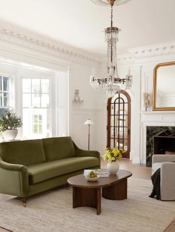 Eclectic living room blending vintage glamour with modern comfort: olive green sofa, wood coffee table, crystal chandelier, and classic fireplace