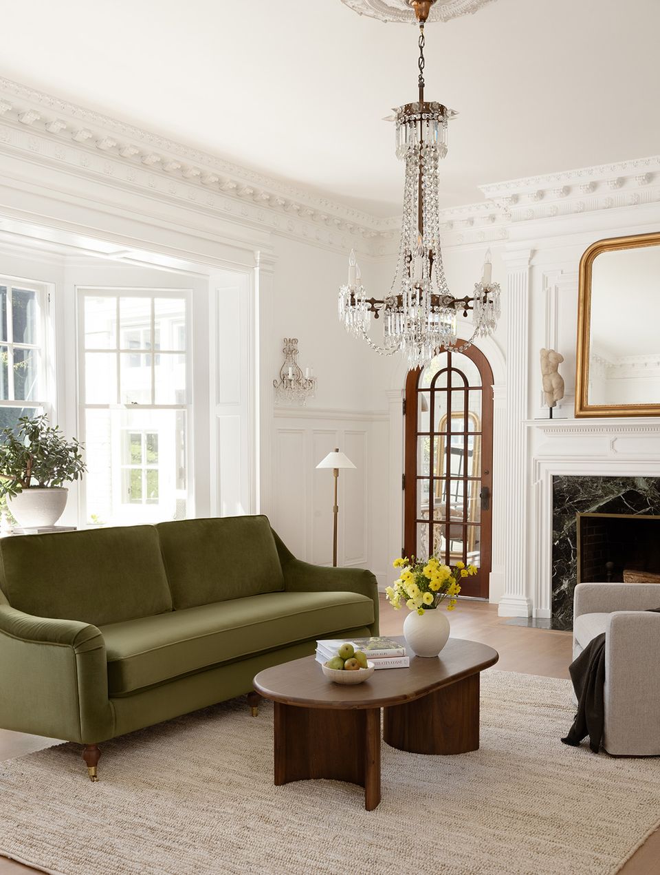 Eclectic living room blending vintage glamour with modern comfort: olive green sofa, wood coffee table, crystal chandelier, and classic fireplace
