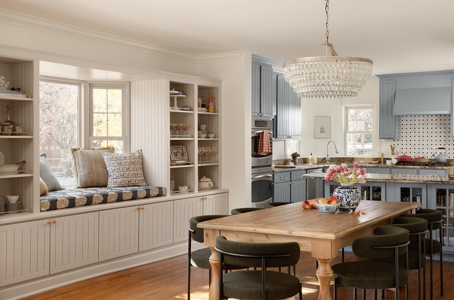 Bright transitional kitchen with soft blue cabinetry, beaded chandelier, and cream window seat with storage