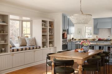 Bright transitional kitchen with soft blue cabinetry, beaded chandelier, and cream window seat with storage