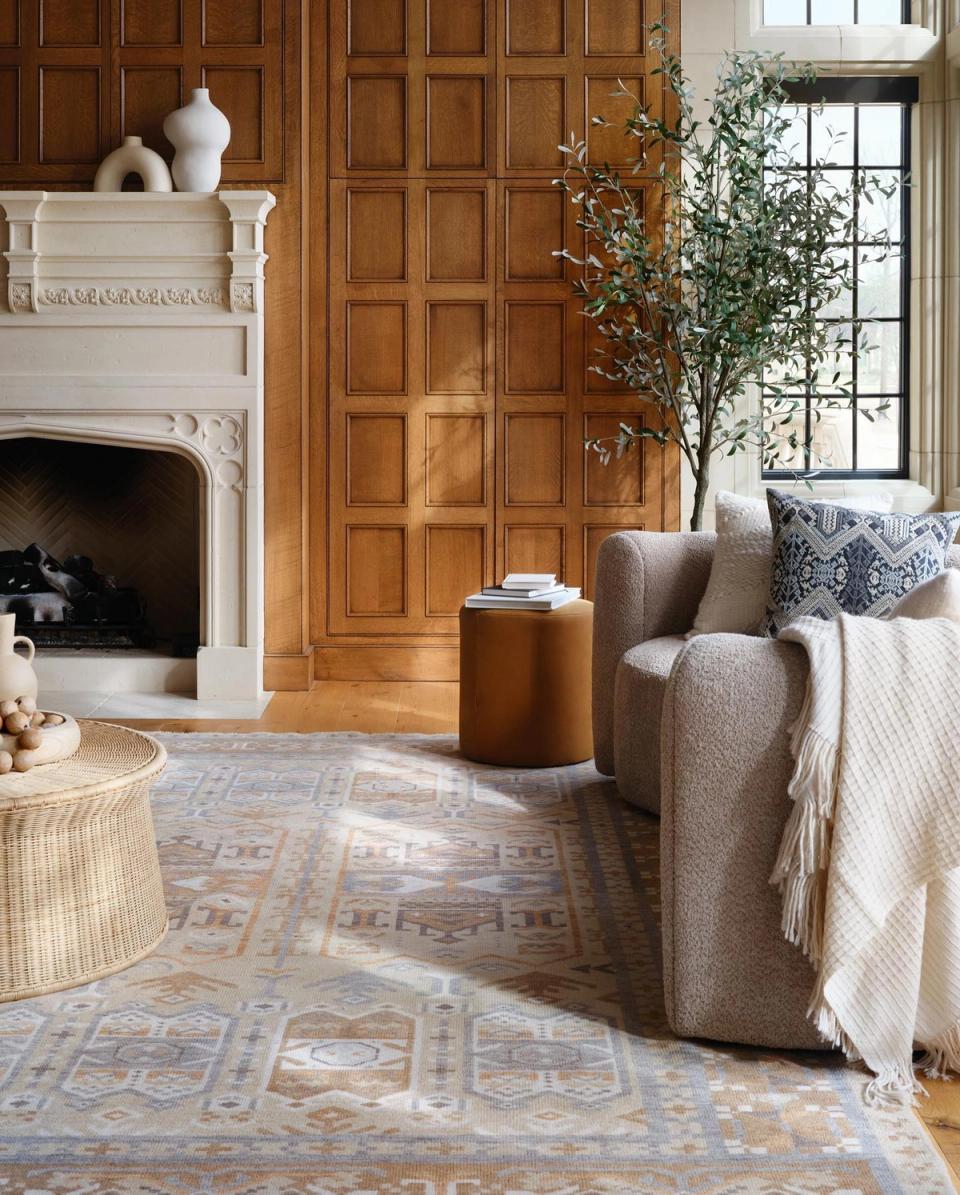 Warm traditional living room with wood paneling, neutral upholstery, fireplace, and patterned area rug